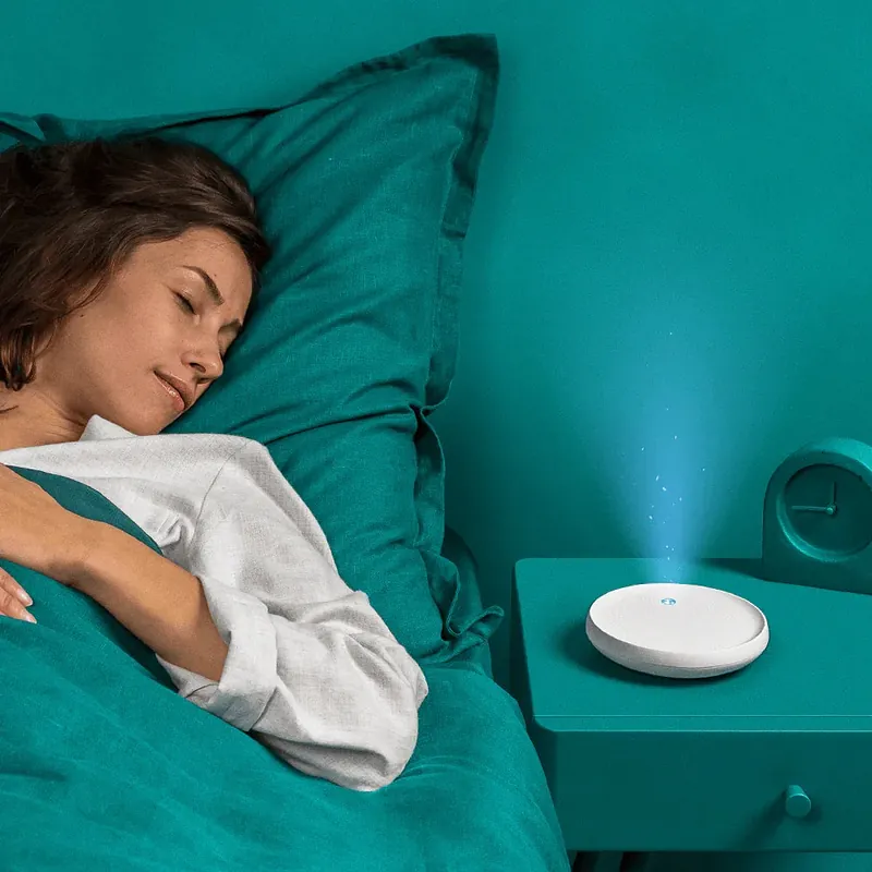Dodow on a bedside table, its blue light glowing beside someone asleep