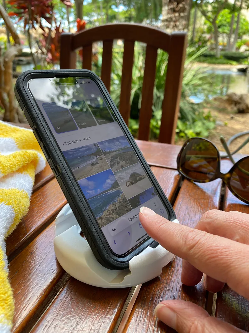 Mão tocando a tela do celular encaixado no GoDonut branco, sobre mesa de madeira ao ar livre