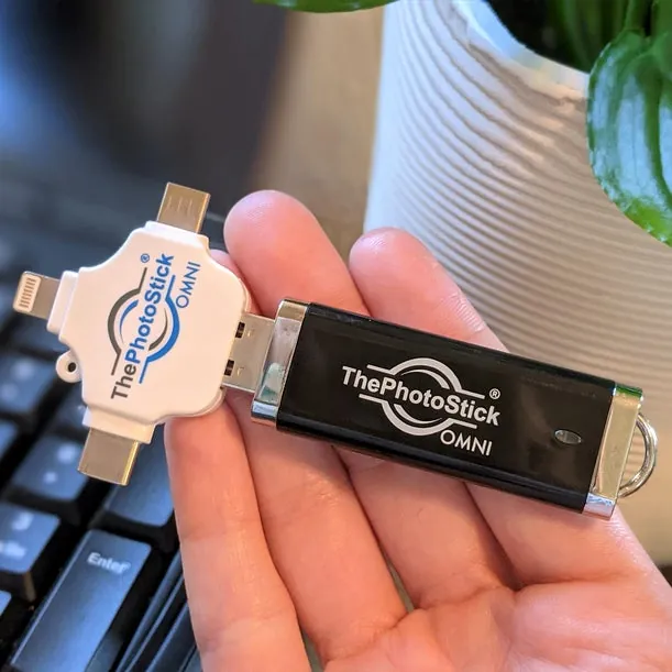Mão segurando o ThePhotoStick OMNI e o conector de três pontas sobre um teclado