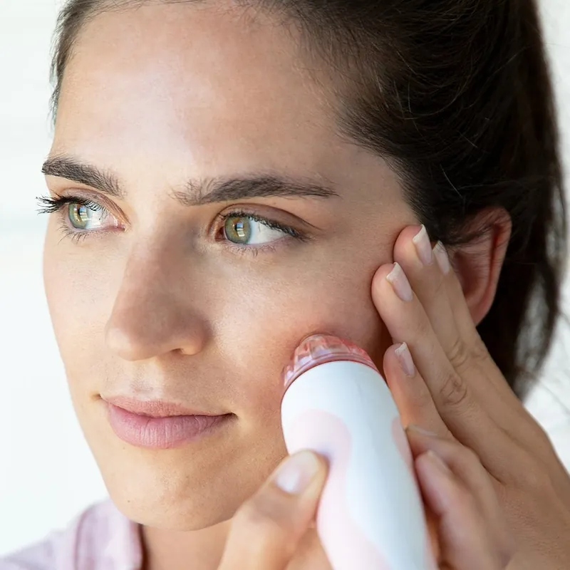 A woman holding the PMD Personal Microderm against her cheek, mid-treatment