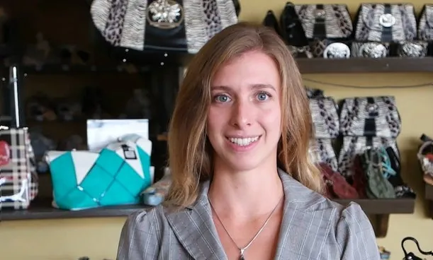 Mulher sorrindo numa loja de calçado, com prateleiras de sapatos ao fundo